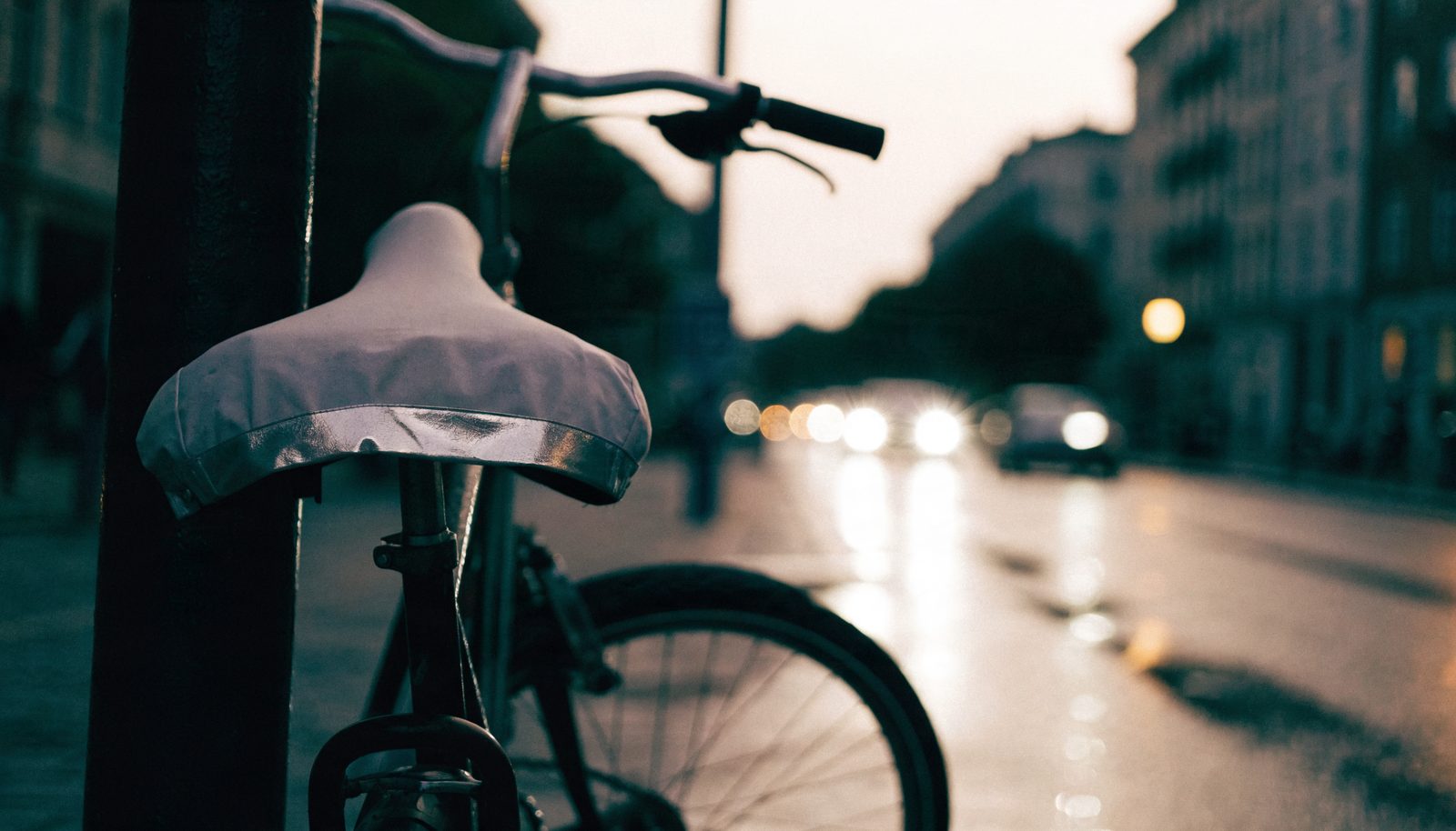 Stadtfahrrad in der Dämmerung mit hellem Sattelbezug und reflektierendem Streifen vor einer regennassen Straße